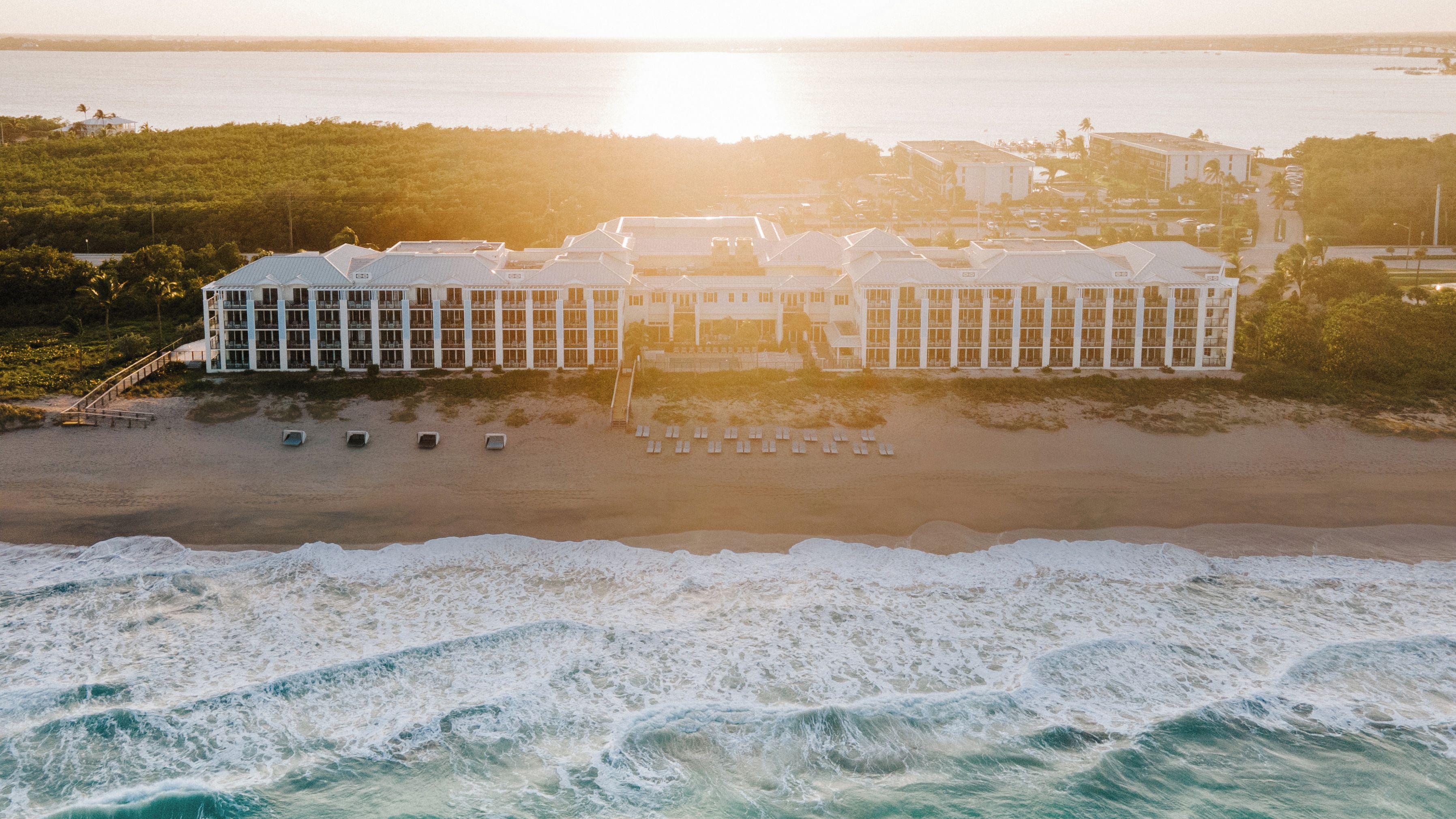 A beachfront hotel with multiple buildings, a sandy beach, and waves crashing onto the shore.