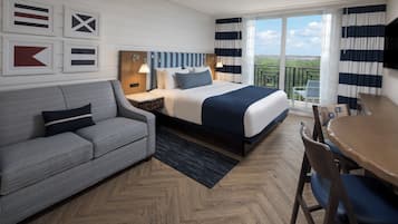 A hotel room with a bed, a sofa, a dining table, and a balcony with a view.
