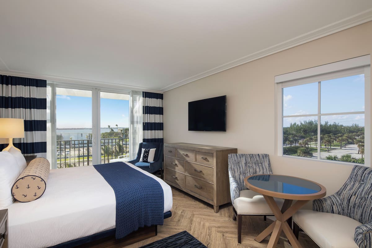 A hotel room with a bed, a desk, a chair, a TV, and a balcony with a view.