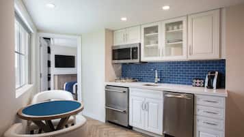 Una cocina moderna con armarios blancos, salpicadero de azulejos azules, electrodomésticos de acero inoxidable y un comedor con mesa azul y sillas blancas.