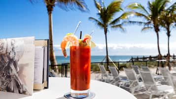 A cocktail with shrimp garnish on a table with a menu and a view of the beach and ocean.
