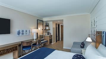 A hotel room with a bed, desk, chair, and a small kitchenette.