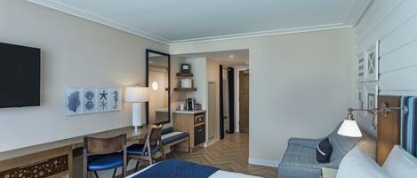 A hotel room with a bed, desk, chair, and a small kitchenette.