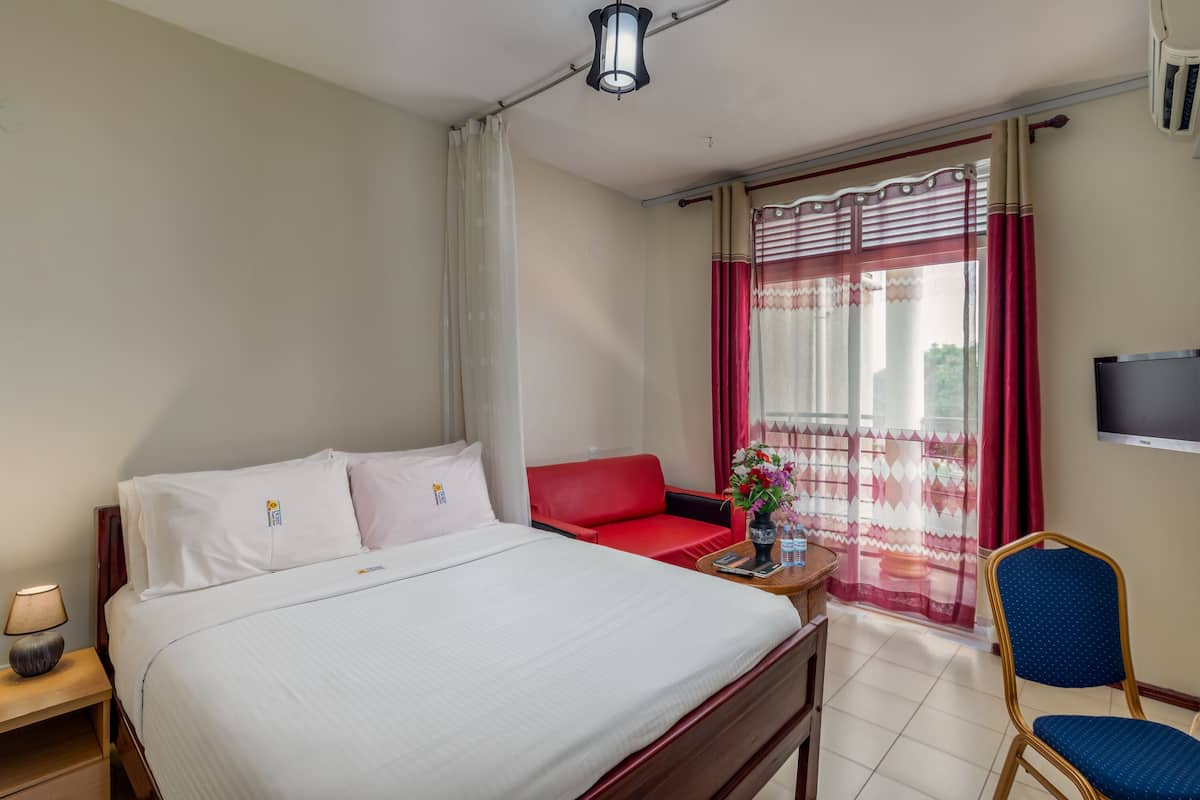A hotel room with a bed, a red sofa, a TV, and a window with curtains.