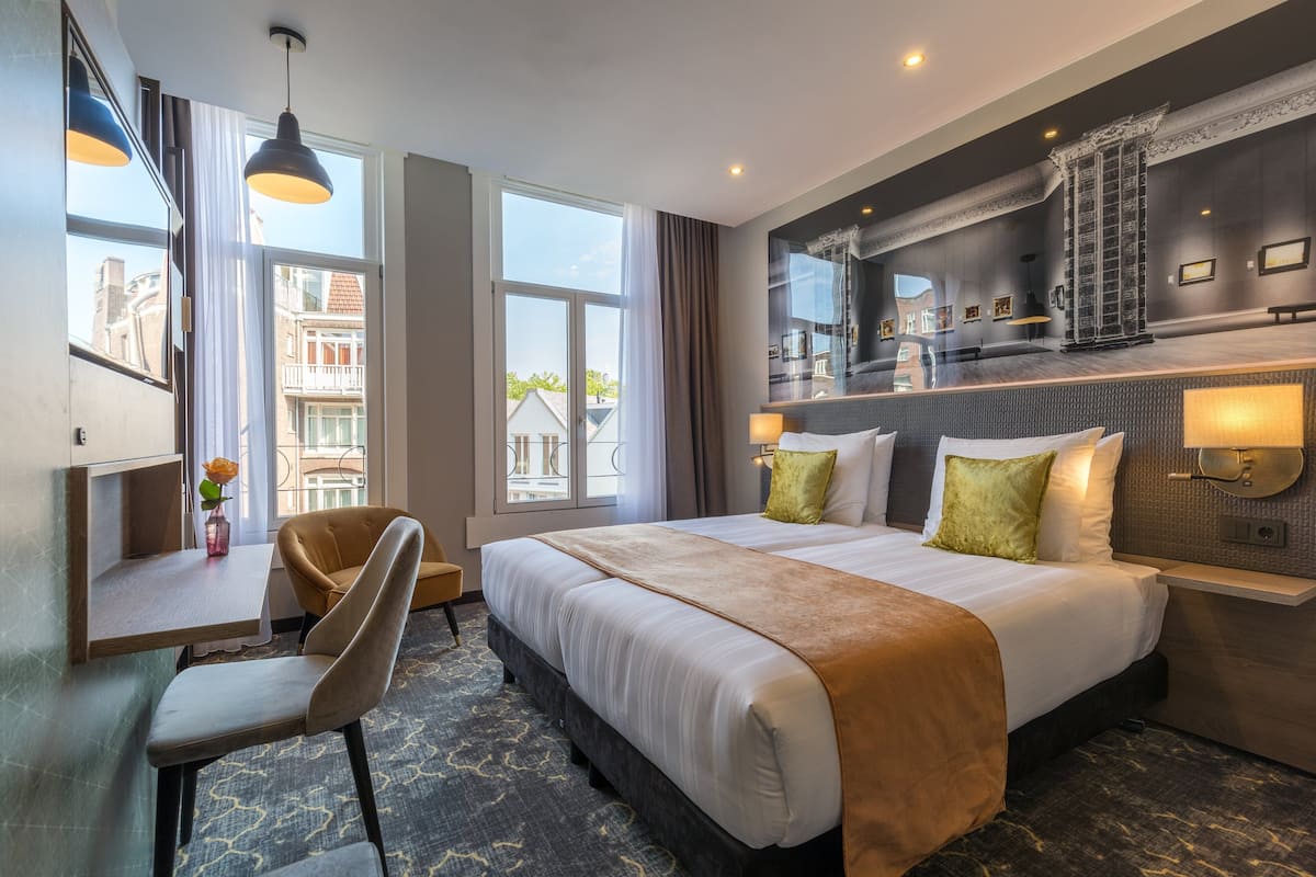 Hotellihuone, jossa on suuri sänky, työpöytä, tuoli ja näkymä kaupunkiin.