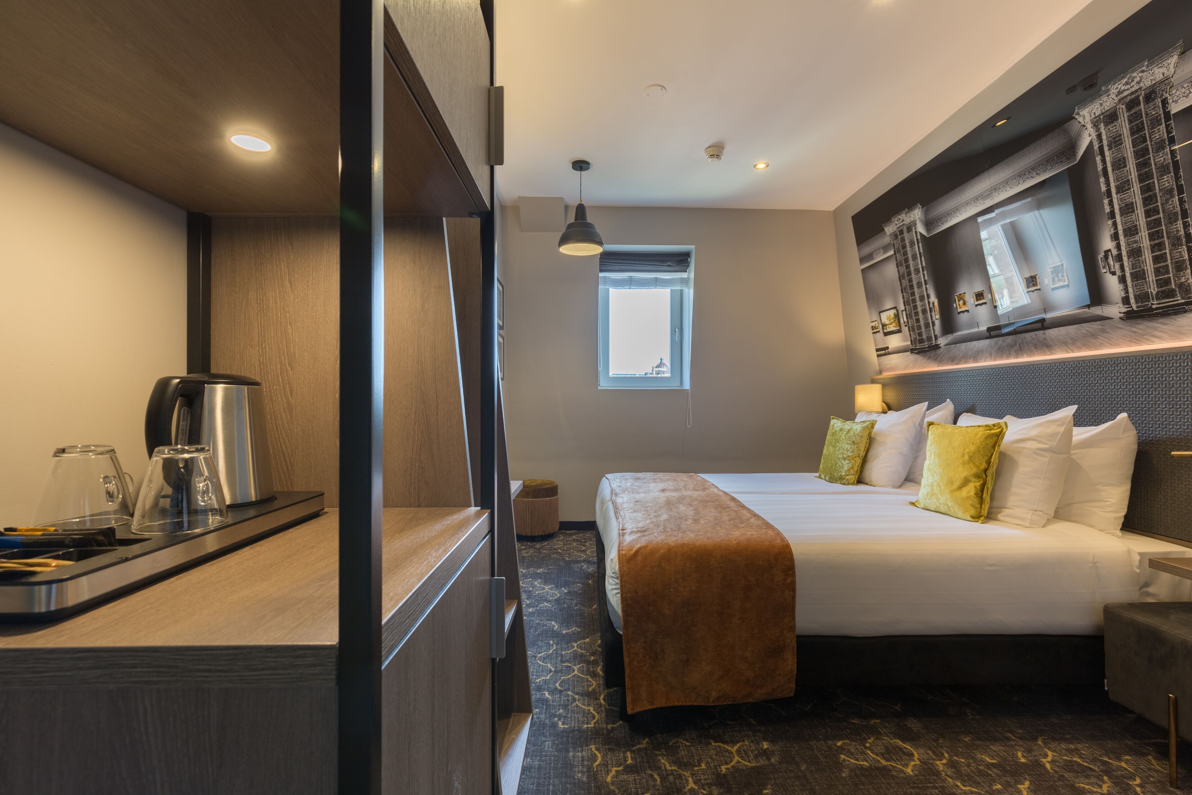 A hotel room with a bed, bedside table, and a window.