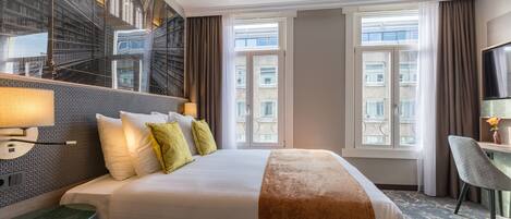 A hotel room with a large bed, a desk, a chair, and a television.