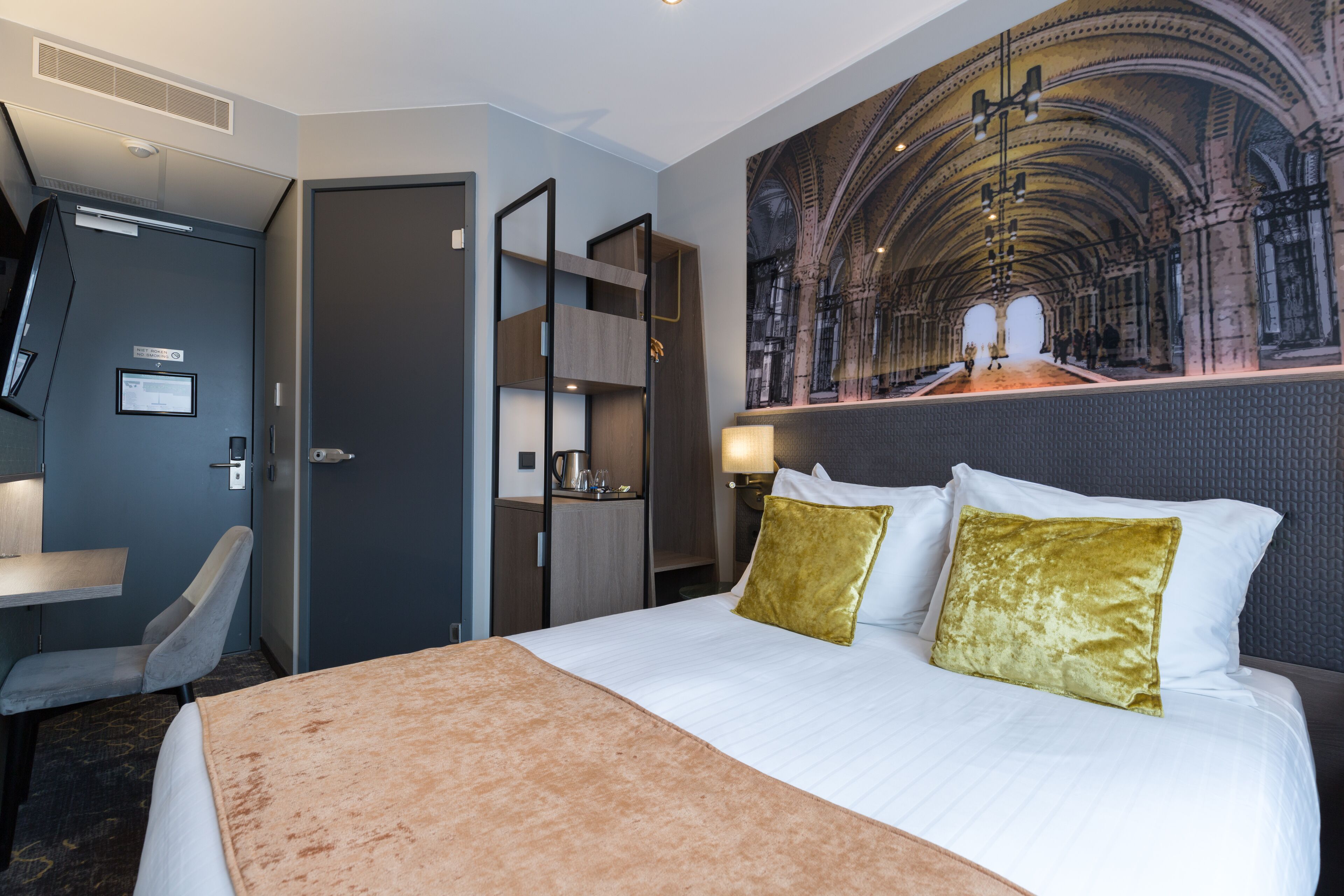Une chambre d’hôtel avec un lit, un bureau, une chaise et une grande fresque murale représentant une cathédrale.