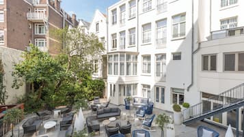 Een binnenplaats met buitenmeubilair, een boom en een gebouw met meerdere ramen en balkons.