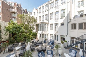 Une cour avec des sièges en plein air, un arbre et un bâtiment doté de nombreuses fenêtres et de balcons.