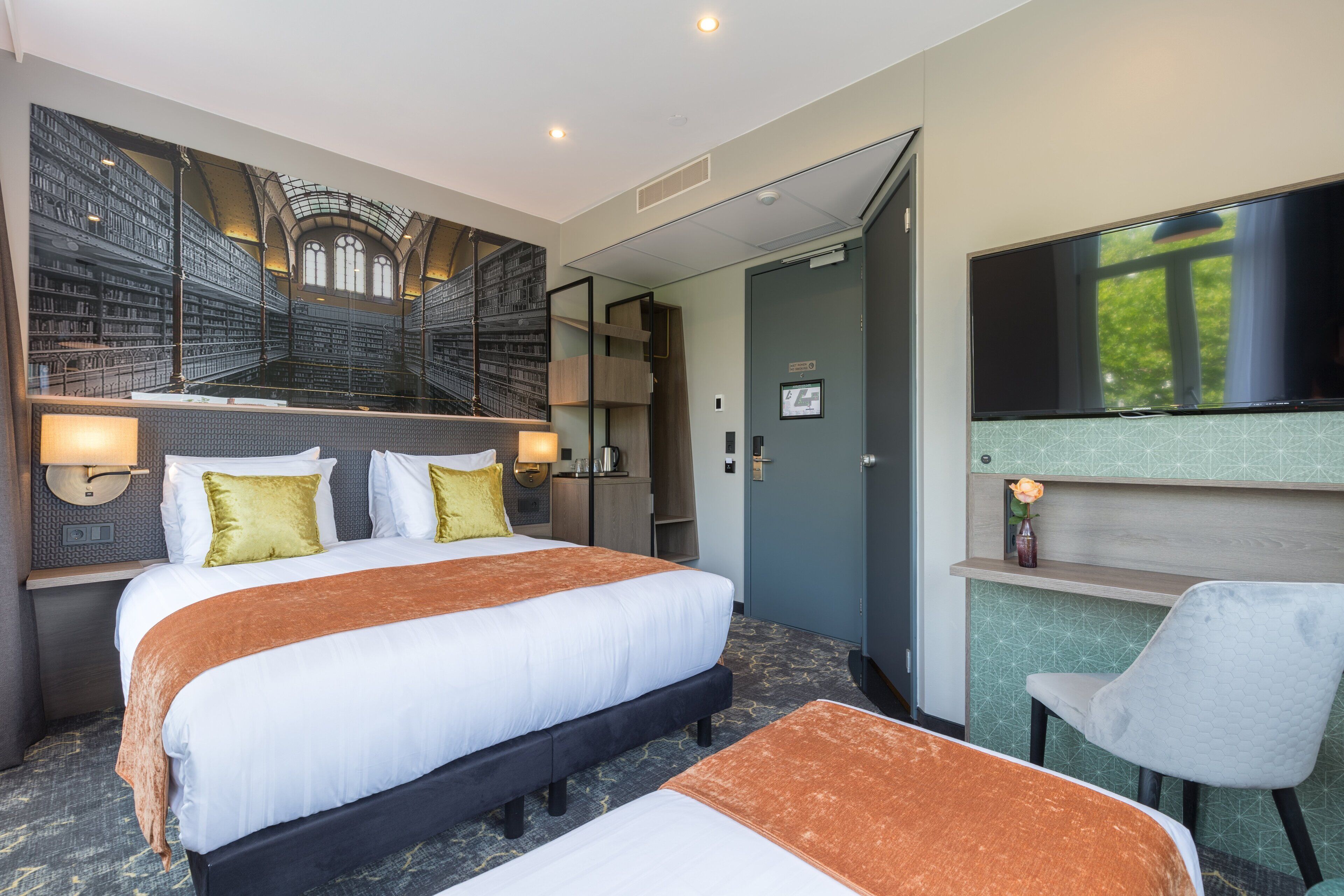 A hotel room with a large bed, a desk with a chair, a flat-screen TV, and a bookshelf.