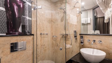 A modern bathroom with a glass-enclosed shower, a white sink, and a marble-tiled wall.