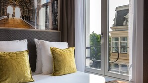 Una habitación de hotel con una cama grande, dos almohadas, un ventanal con vista a un edificio y un mural en la pared.