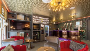 A modern hotel lobby with red sofas, a bar area, and a reception desk.