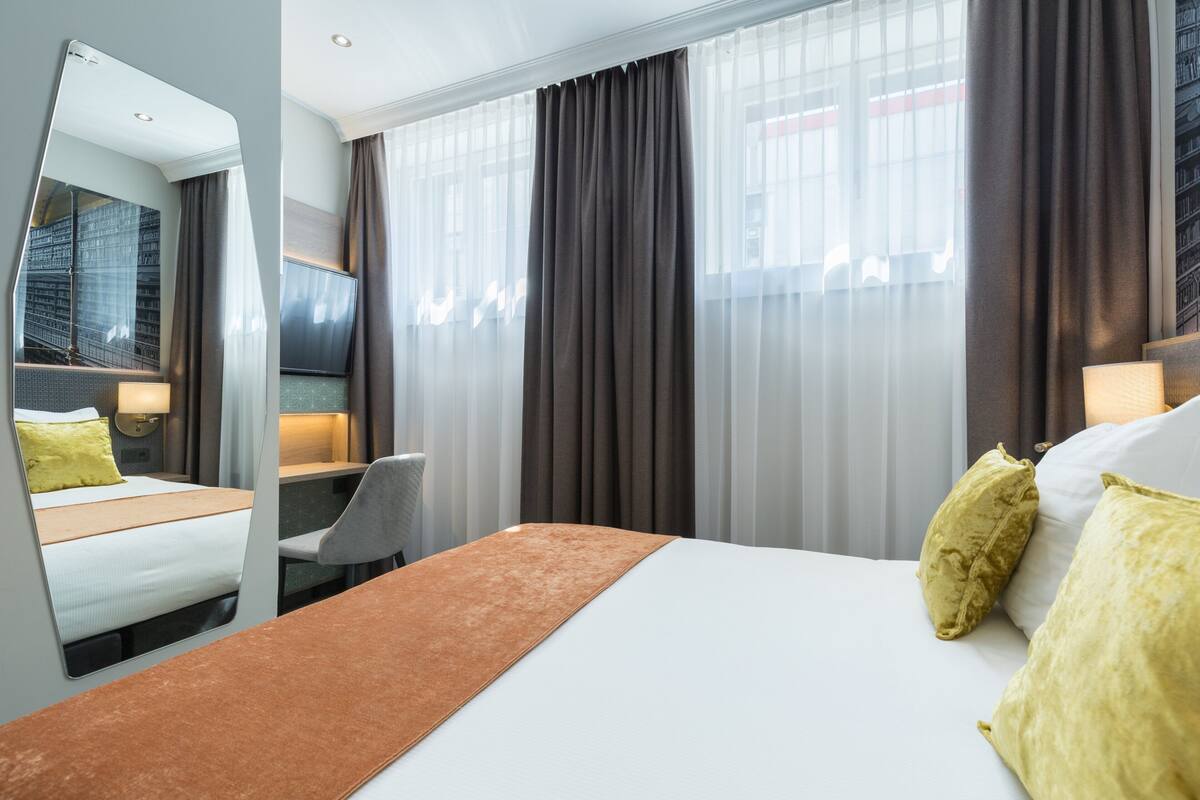 A hotel room with a bed, a desk, a chair, and a large mirror.