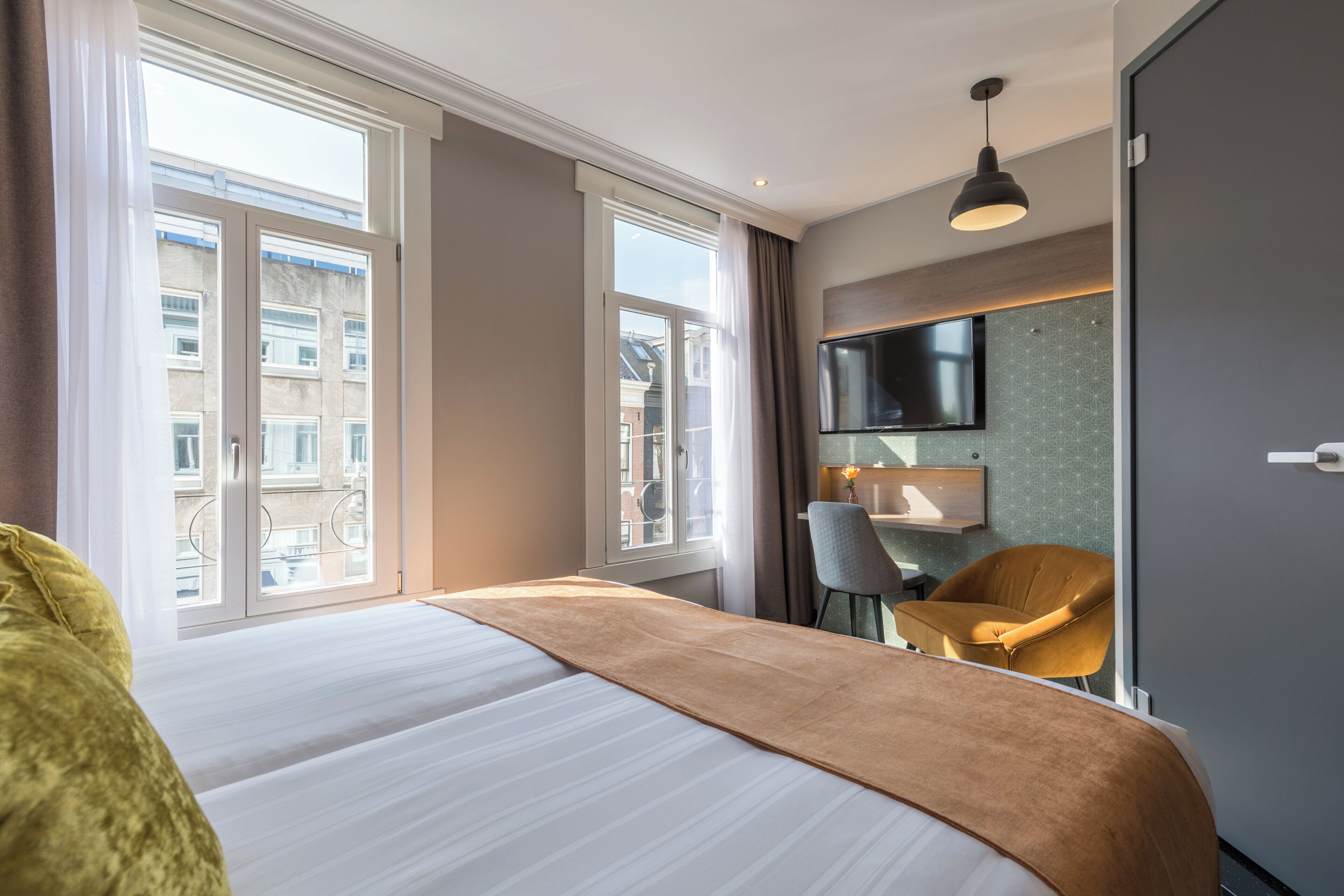 Habitación de hotel con una cama grande, un escritorio, una silla, un televisor y una ventana con cortinas.