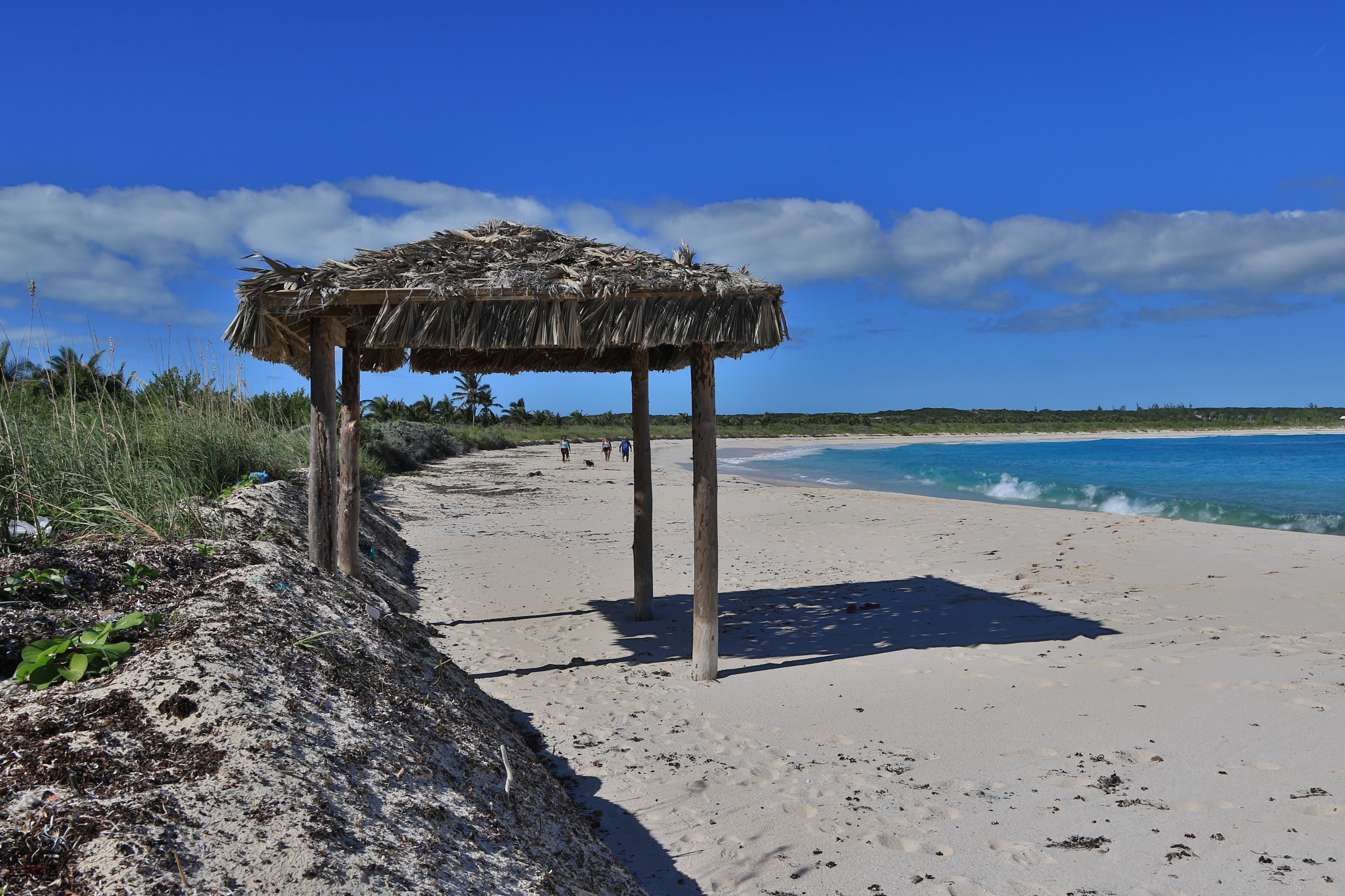 A beach with a thatched structure, clear blue sky, and calm sea.