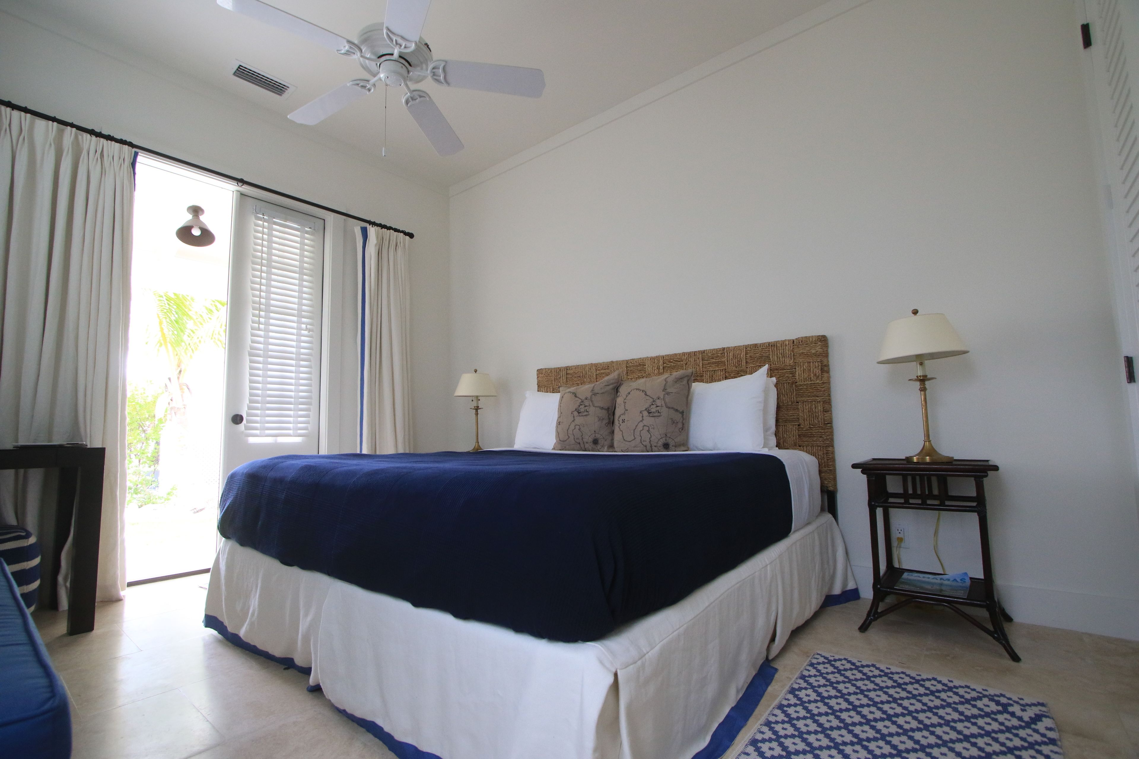 A bedroom with a bed, two bedside lamps, a ceiling fan, a window with curtains, and a small table with a lamp.