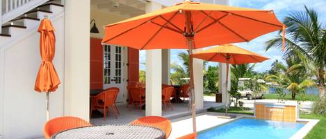 A poolside area with orange wicker furniture and umbrellas, a staircase, and a view of the pool and palm trees.