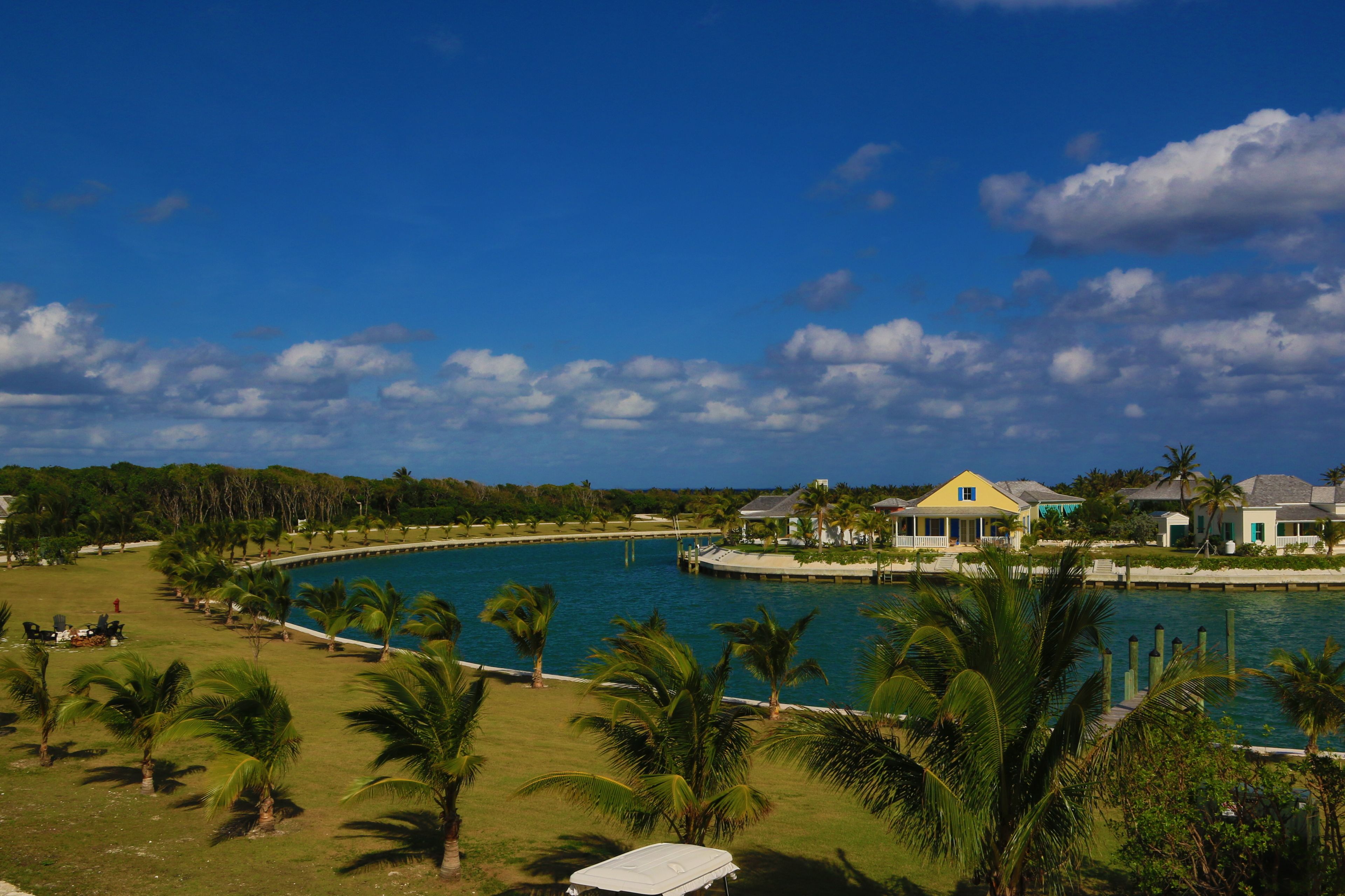 A coastal property with a pool, palm trees, and a yellow house.