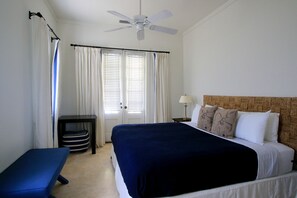 A hotel room with a bed, a bench, a ceiling fan, a nightstand, and a lamp. - The Sandpiper Inn & Cottages (Crossing Rocks)