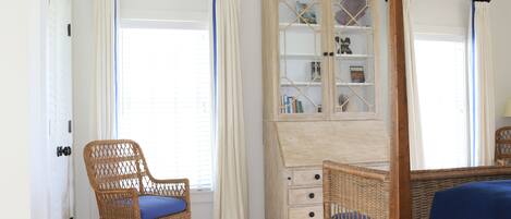 A room with a wicker chair, a cabinet with drawers, and a bed with a blue mattress.
