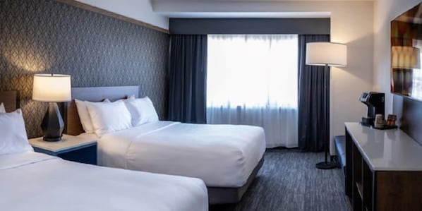 Habitación de hotel con dos camas, un escritorio, una lámpara y vista a la ciudad.
