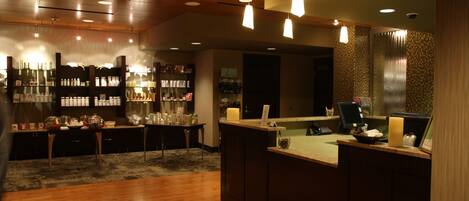 A bar area with wooden flooring, a counter with a cash register, and shelves stocked with bottles.
