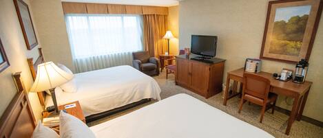 A hotel room with two beds, a desk, a television, and a painting on the wall.
