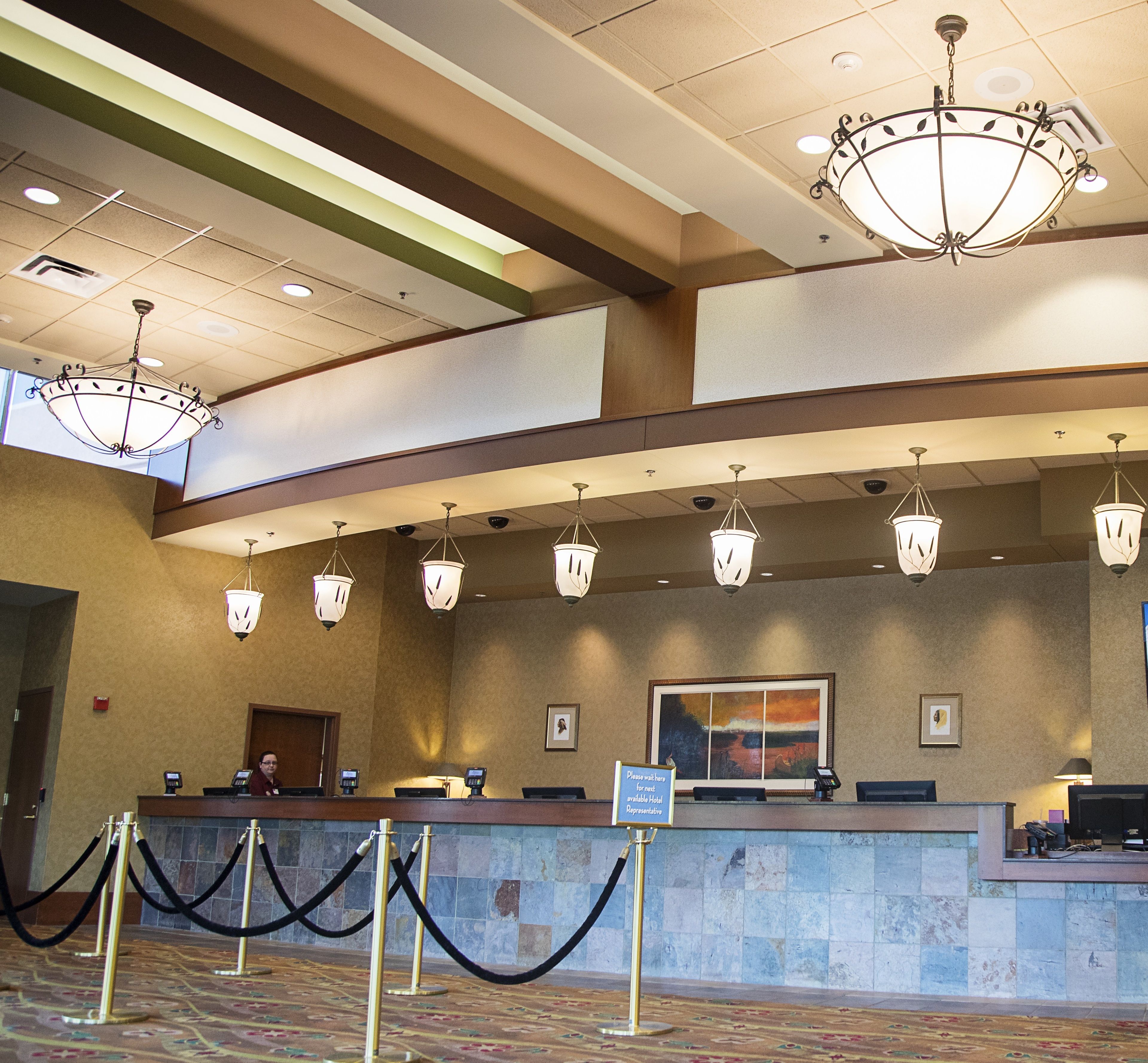 A hotel reception area with a counter, multiple chandeliers, a large painting on the wall, and a sign indicating a waiting area for hotel representatives.