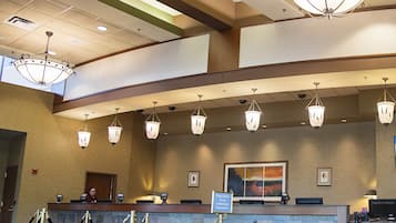 A hotel reception area with a counter, multiple chandeliers, a large painting on the wall, and a sign indicating a waiting area for hotel representatives.