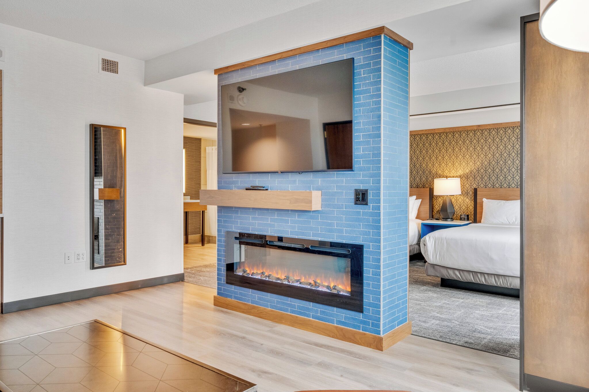A modern hotel room with a fireplace, a large mirror, and a bed with a headboard.