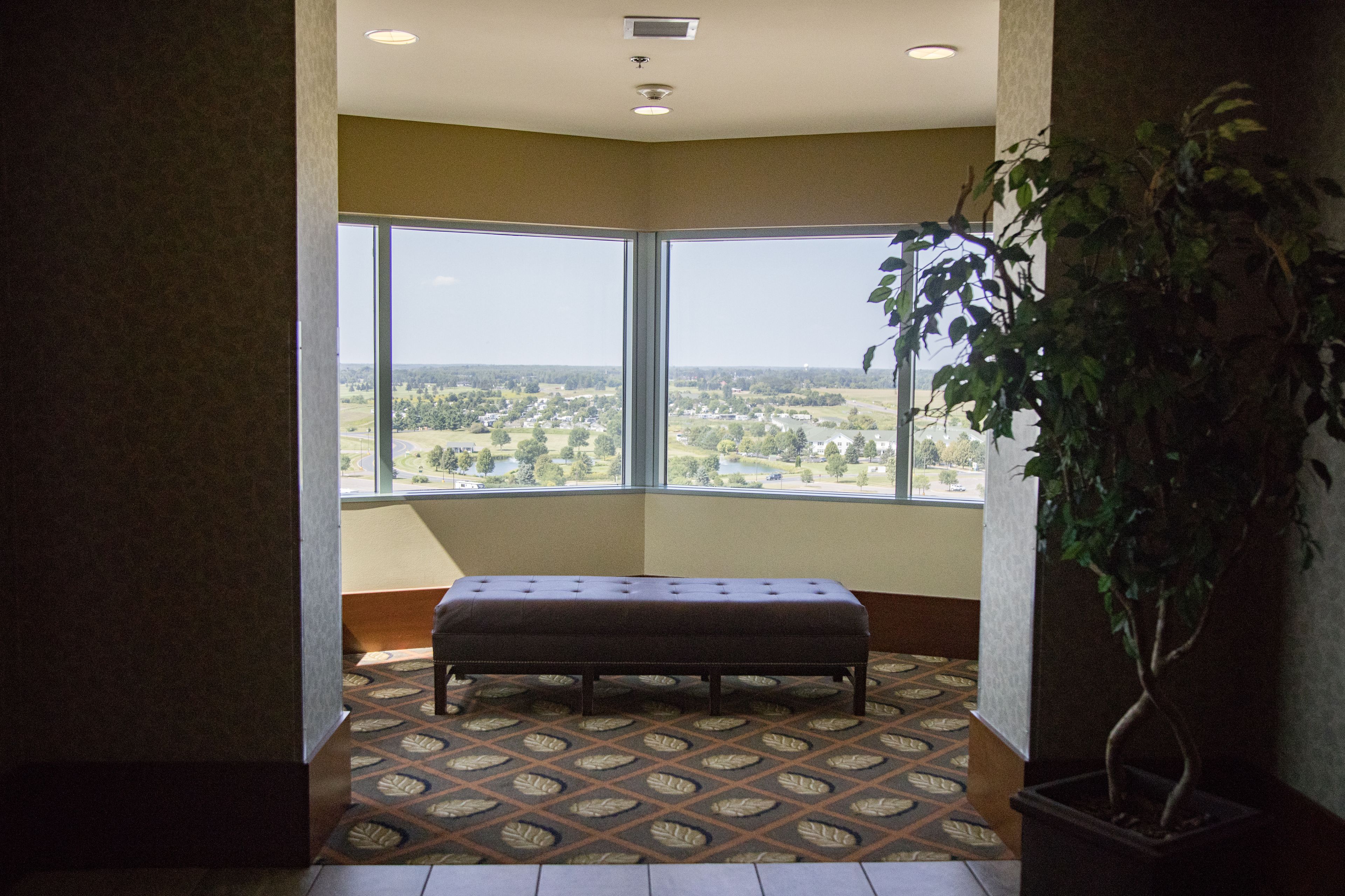 Quarto de canto com uma janela ampla que oferece vista para a paisagem, um banco e um vaso com planta.