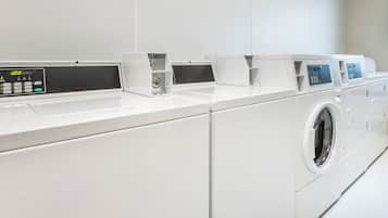 A row of white, modern, front-loading washing machines in a clean, white-walled laundry room.