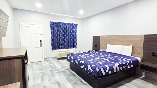 A modern hotel room with a bed, a desk, a TV, and a window with curtains. - Airway Inn - IAH Airport (Houston)