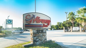 A sign for the Airway Inn, featuring a stone pillar and a clear view of the parking area with cars and a gas station in the background. - Airway Inn - IAH Airport (Houston)