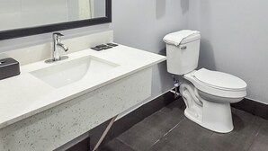 A modern bathroom with a white sink, a mirror, a toilet, and a towel rack. - Airway Inn - IAH Airport (Houston)