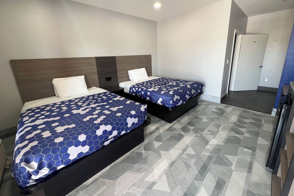 A hotel room with two beds, each with a patterned bedspread, a headboard, and a bedside table.