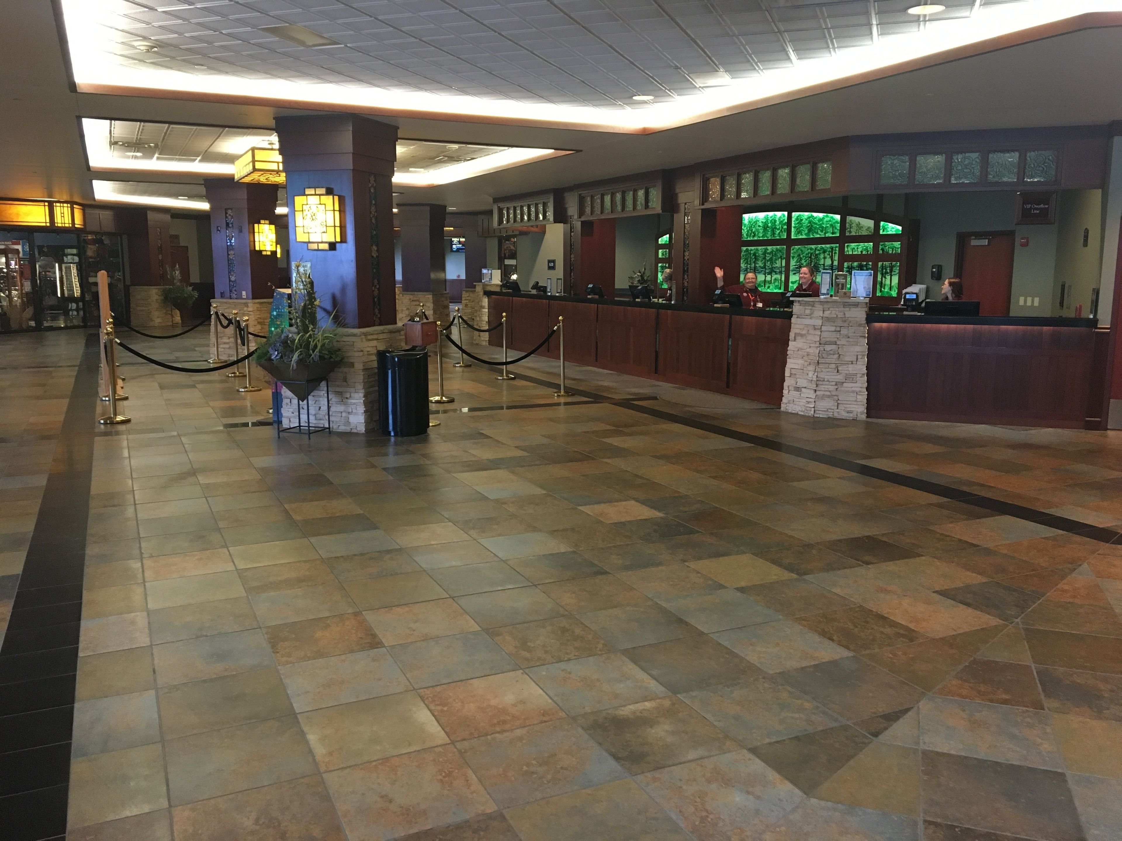 A spacious lobby with a check-in counter, a reception desk, and a seating area with a potted plant.