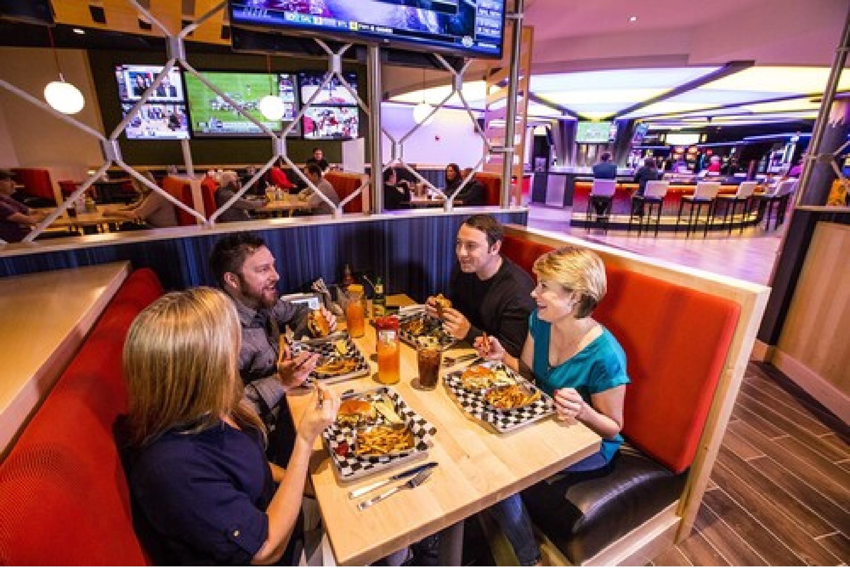 A group of people dining at a restaurant with multiple screens displaying sports events in the background.