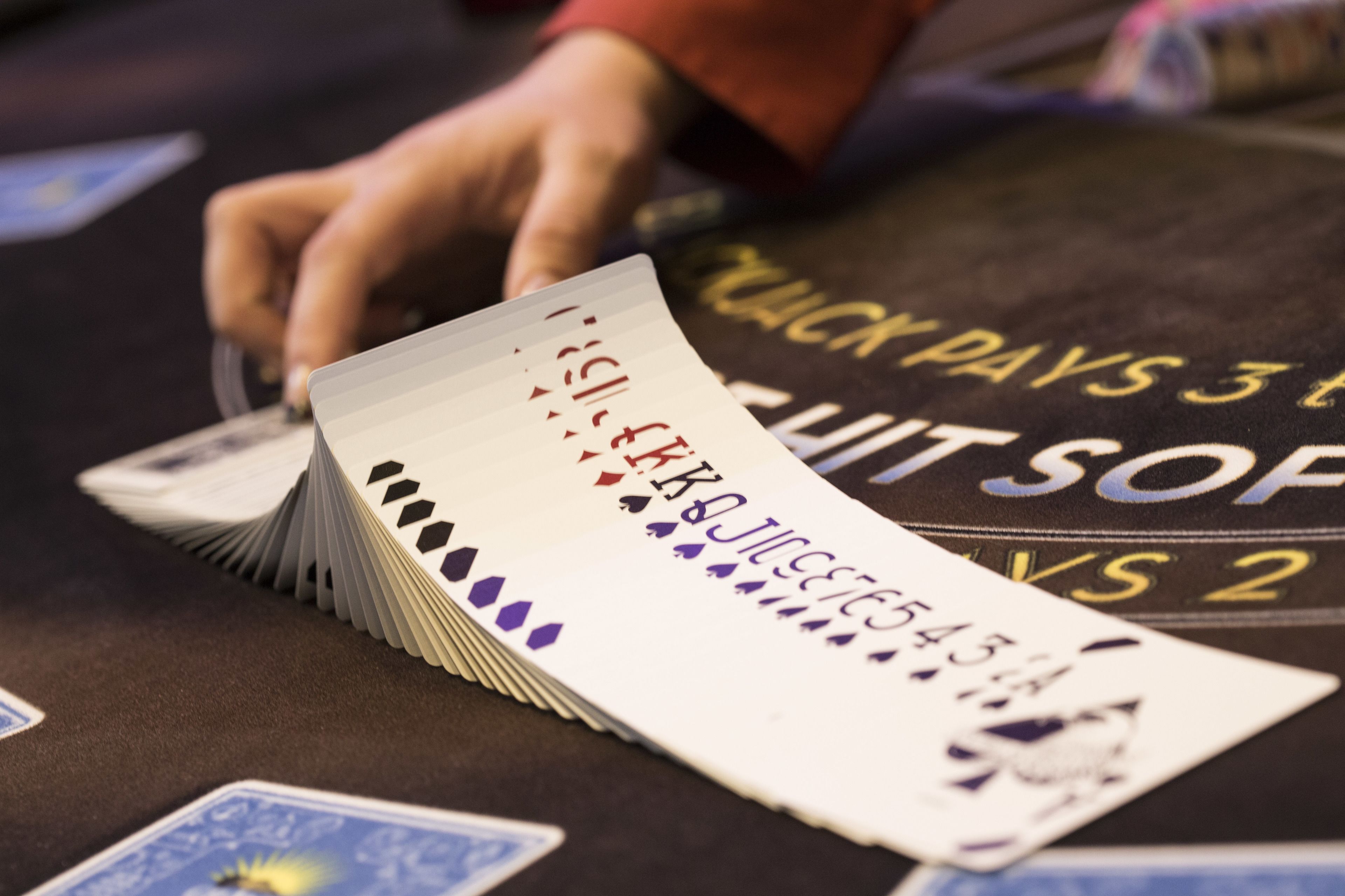 A hand shuffling playing cards on a table with a visible text that reads "BLACK PAYS 3 TO WHITE SOFT."