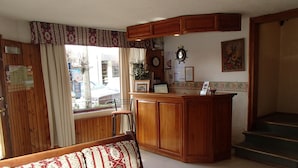 A cozy living area with a wooden bench, a kitchen with wooden cabinets, a window with curtains, and a staircase. - Hosteria Sur (San Carlos de Bariloche)