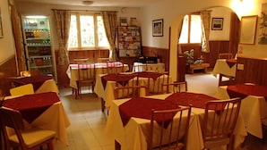 A dining area with tables and chairs, a refrigerator with beverages, and a bookshelf. - Hosteria Sur (San Carlos de Bariloche)