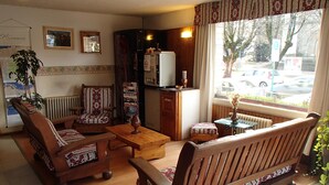 A cozy living room with a sofa, armchair, and a small table. There is a radiator, a cabinet, and a window with a view of the street. - Hosteria Sur (San Carlos de Bariloche)