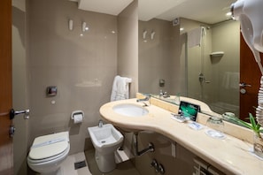 A modern bathroom with a beige sink, a bidet, a toilet, and a glass shower enclosure.