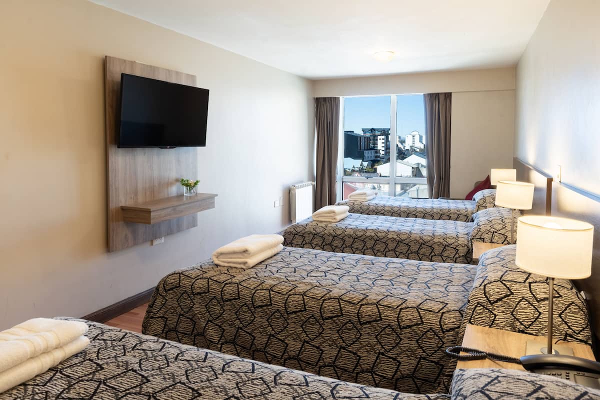 Habitación de hotel con dos camas, un televisor montado en la pared, una ventana con cortinas y vistas a edificios.