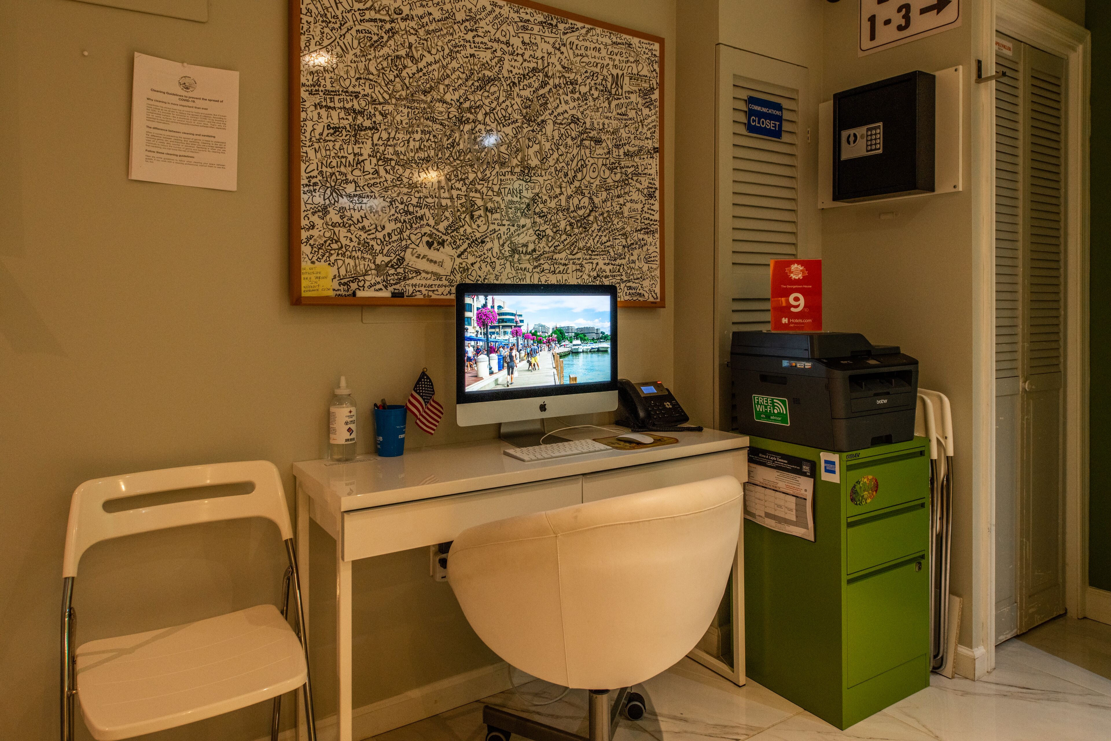 A hotel room with a desk, a computer, a chair, a green filing cabinet, and a wall with a large, hand-written message.