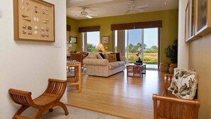 A spacious living room with a sofa, wooden chairs, and a coffee table. There is a framed picture on the wall and a ceiling fan. - Kumulani F 2 (Kamuela)