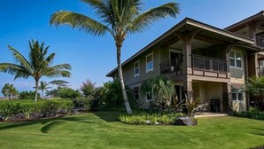Een huis met twee verdiepingen en een balkon, omgeven door een verzorgd gazon en palmbomen.