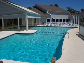 A swimming pool with clear blue water, surrounded by lounge chairs and a covered area. - Lake Arrowhead Respite (Myrtle Beach)